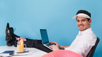 man in glasses and cap works on isolated background. guy posing with laptop, cocktail and inflatable circle.